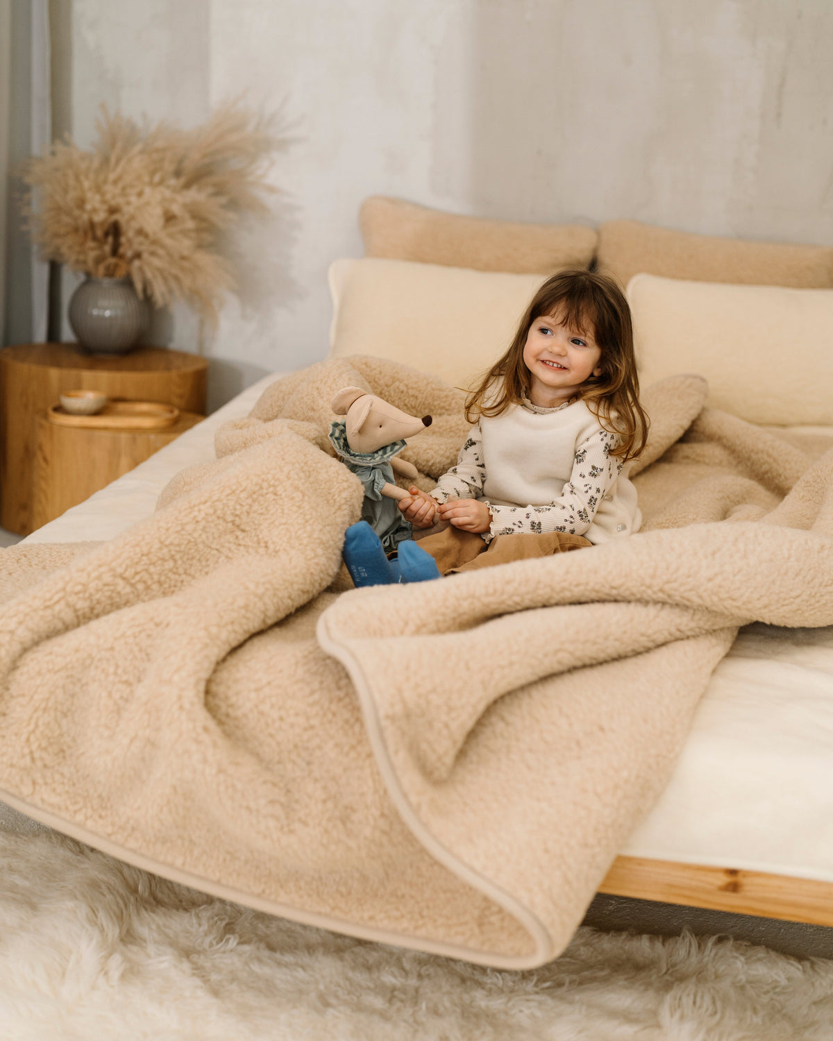 A child playing on a bed with the Nut merino blanket