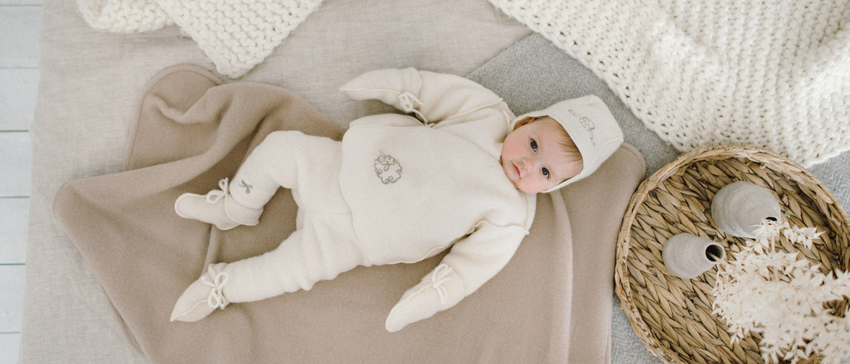Baby in a merino romper, hat and booties on a soft blanket