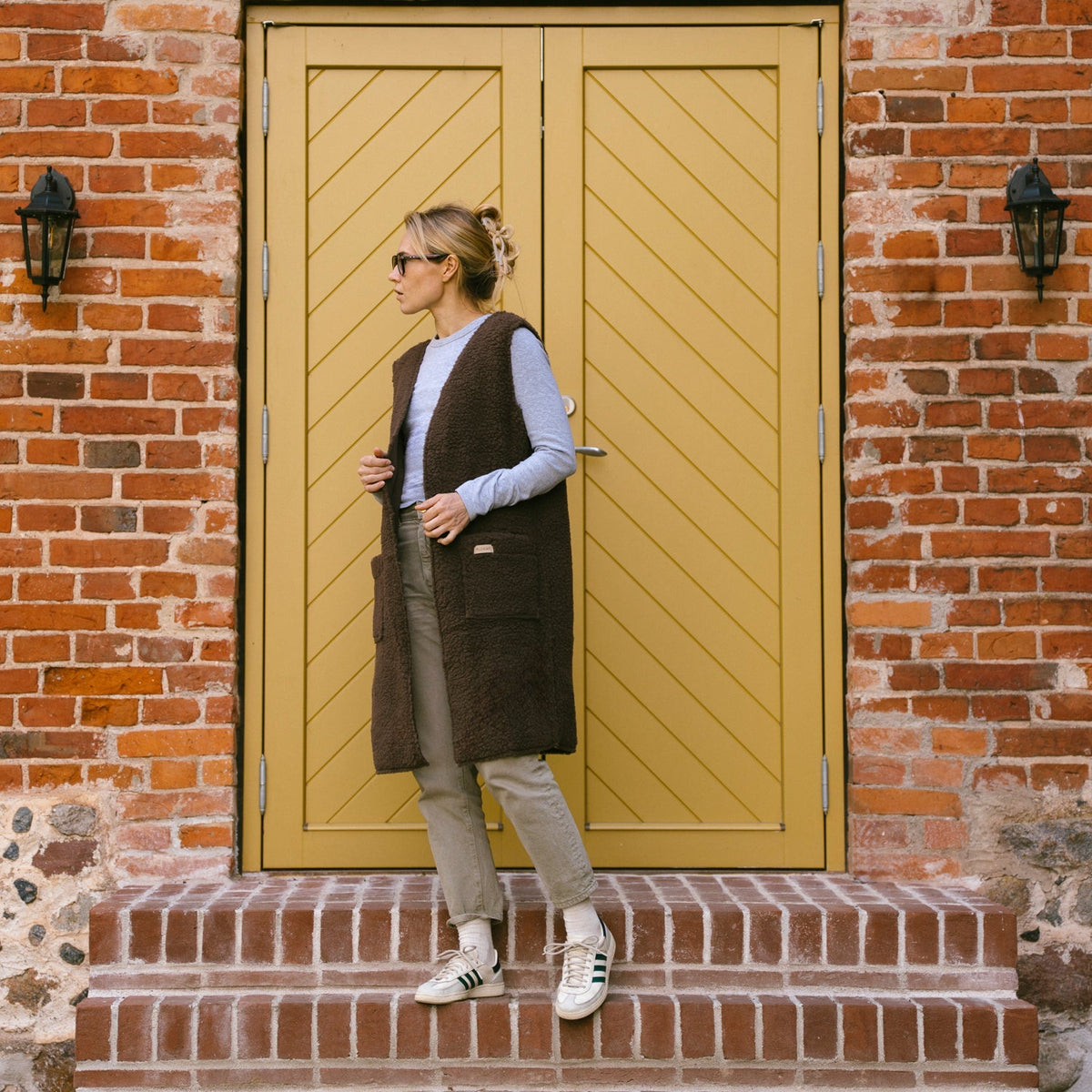 The brown Sea merino vest in front of a yellow door