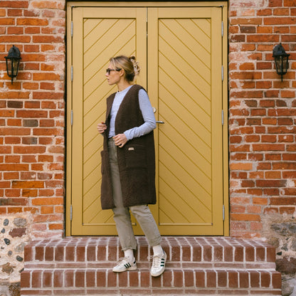 The brown Sea merino vest in front of a yellow door