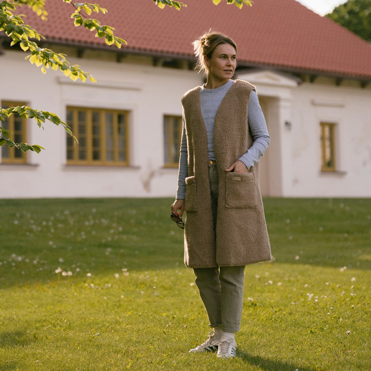 The long beige Sea merino vest, full length, in a garden
