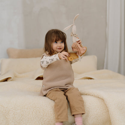 A child sitting on a bed with the Marzipan merino blanket