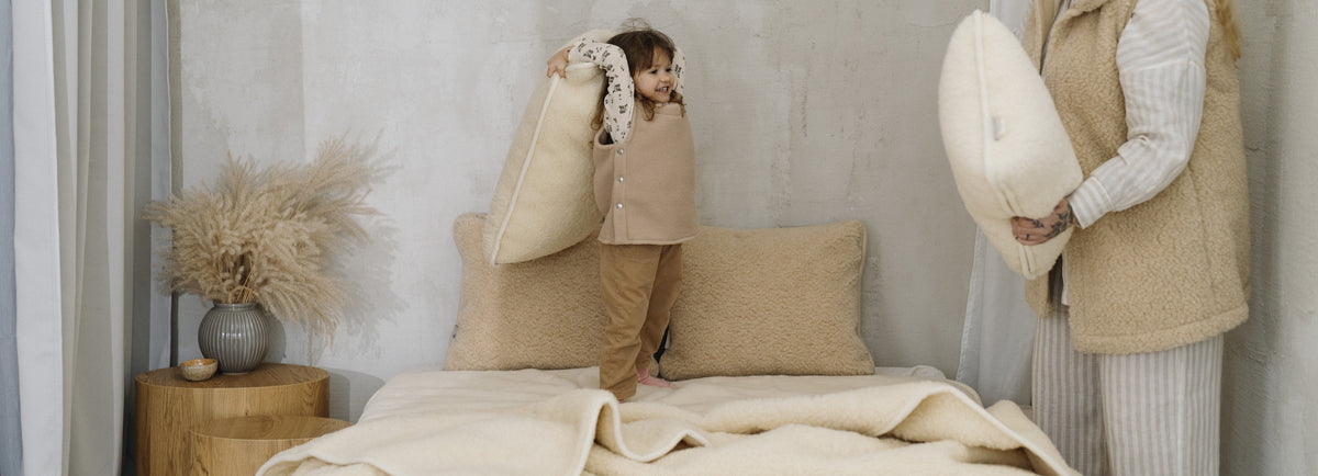 Child playing with wool pillows on a bed with a merino wool blanket