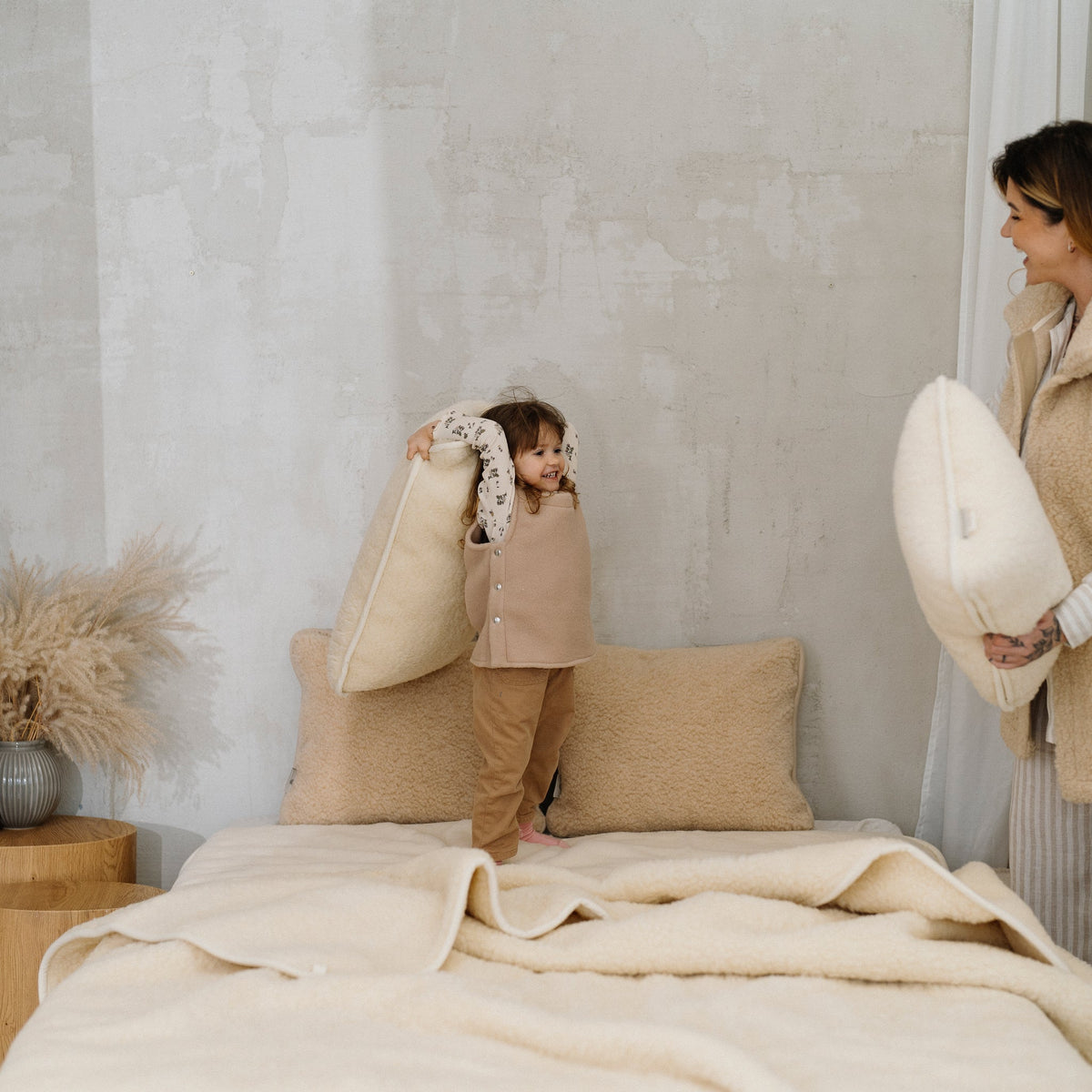 A woman and a child playing on a bed with the Marzipan merino blanket