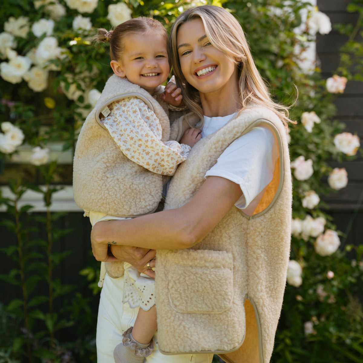 A woman holding a child, wearing the beige Island merino vest