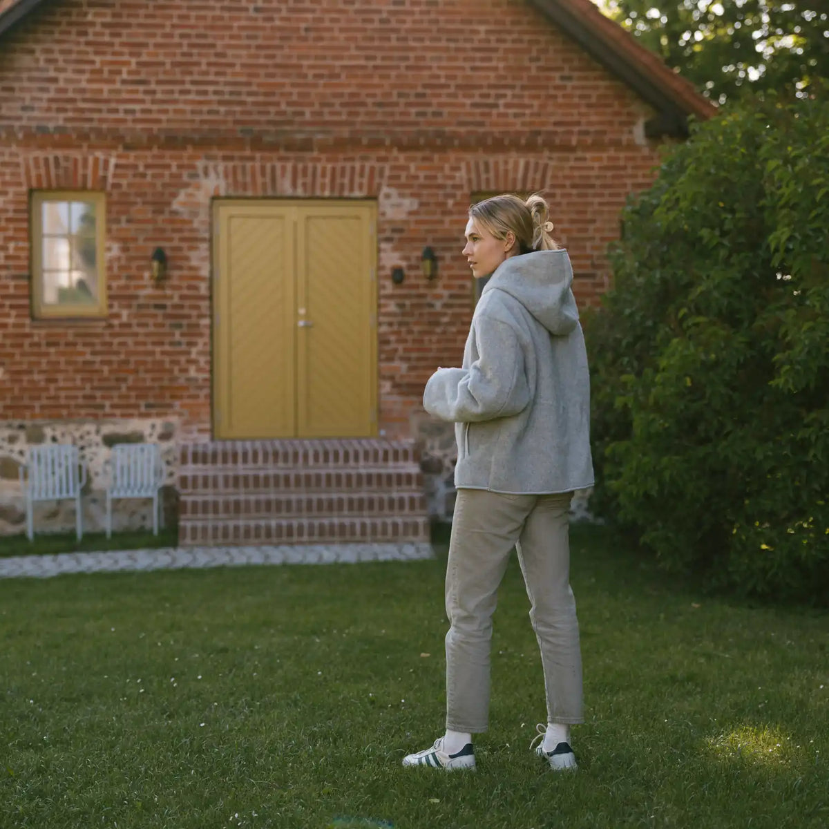 A woman in the grey Laguna merino jacket in front of a brick house