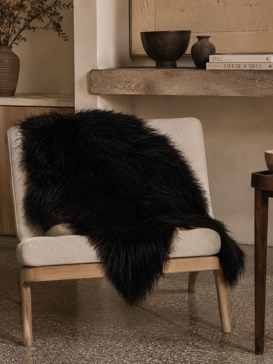 Black Icelandic sheepskin draped over a wooden lounge chair