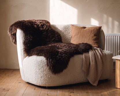 Brown sheepskin rug and a cushion on a bouclé armchair