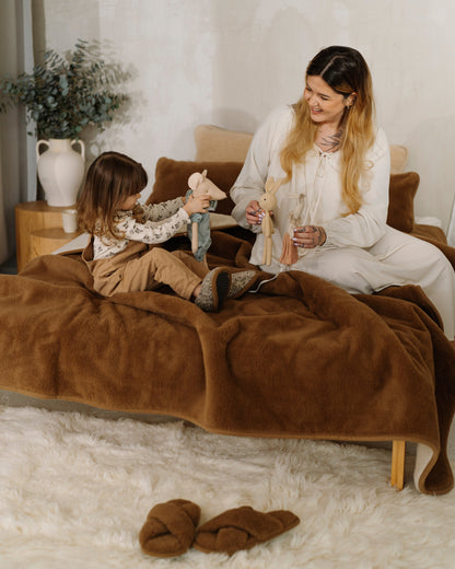 An adult and a child sitting on a bed with the Camel wool blanket