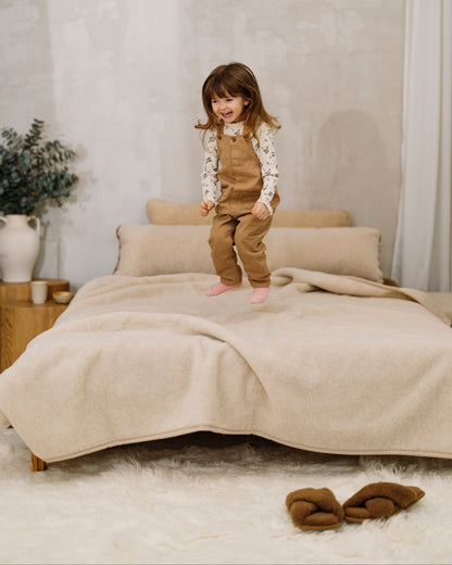 A child standing on a bed made with the Caramel wool blanket