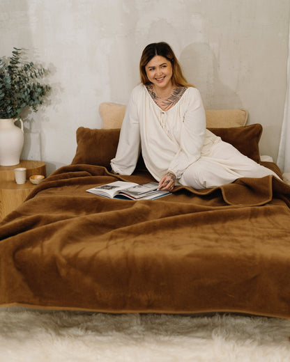 A woman sitting on a bed with the Chocolate wool blanket