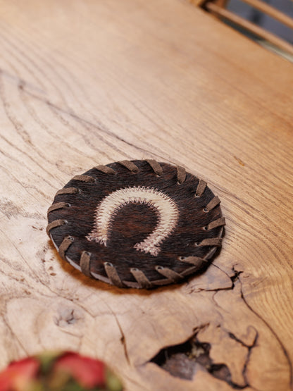 A cowhide coaster with a horseshoe on a wooden table, close up