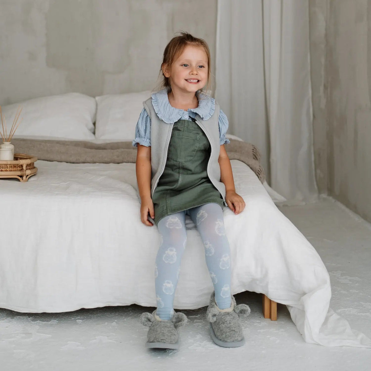 A child sitting on a bed in Mouse merino slippers