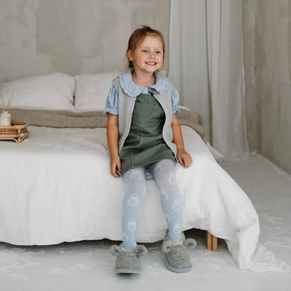 A child sitting on a bed in Mouse merino slippers