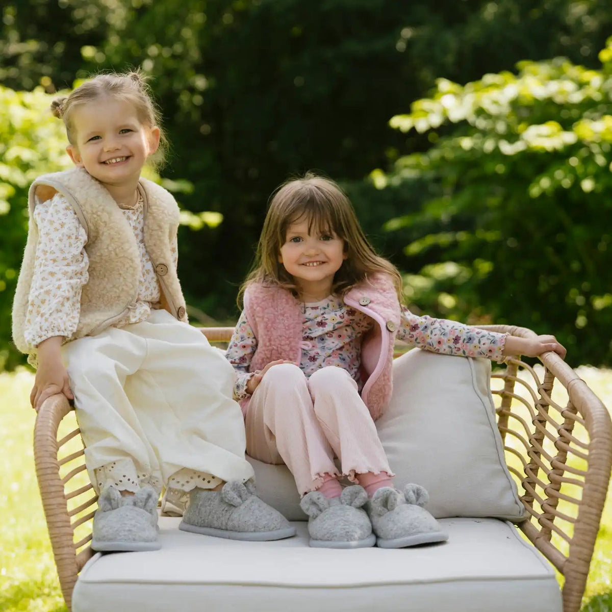 Two children on a garden bench in merino slippers and vests