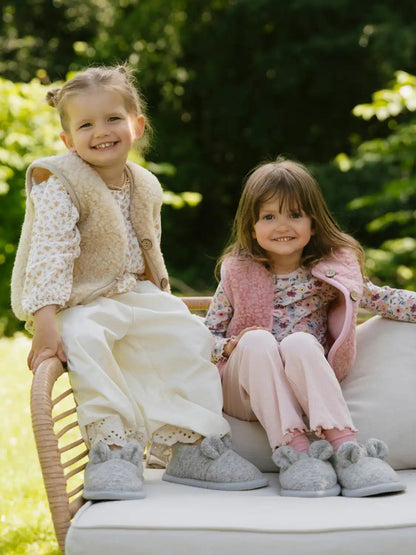 Two girls on a garden bench wearing merino vests