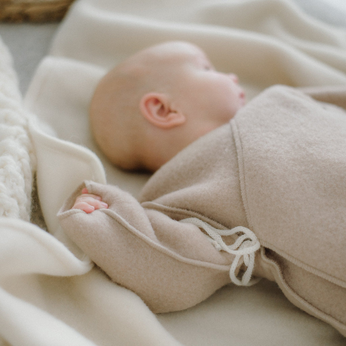 A baby resting in the beige merino jacket