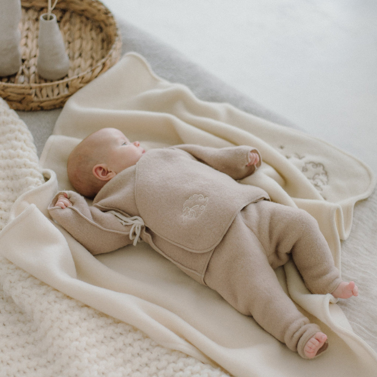 A baby lying on a blanket in the beige merino trousers