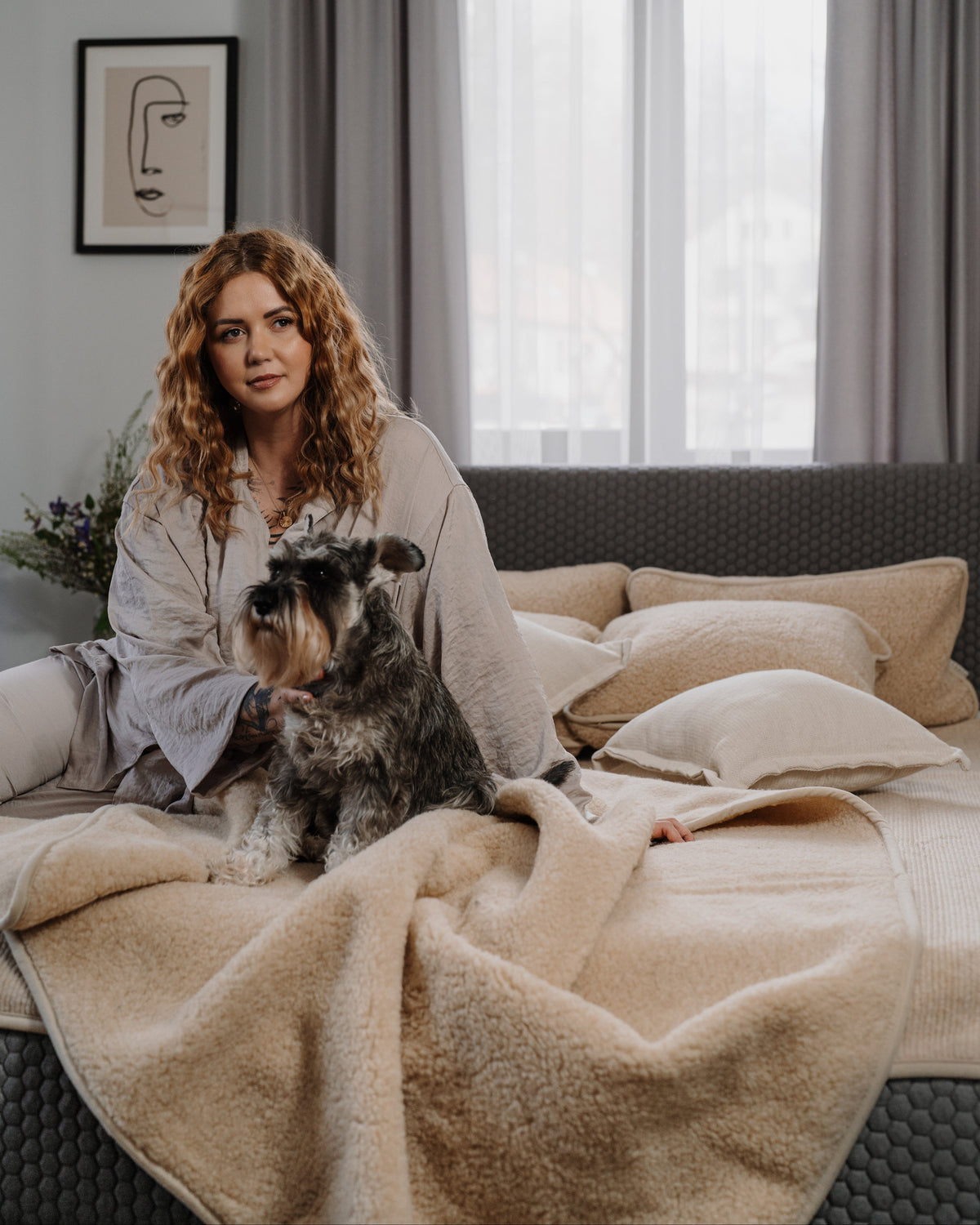 A woman and her dog relaxing on a bed with the Almond merino blanket