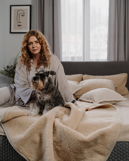 A woman and her dog relaxing on a bed with the Almond merino blanket