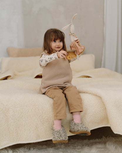 A child sitting on a bed with the Luka merino blanket