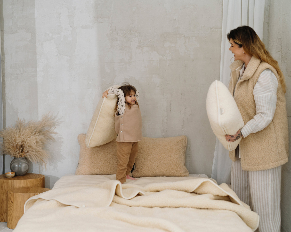 A woman and a child playing on a bed with the Luka merino blanket