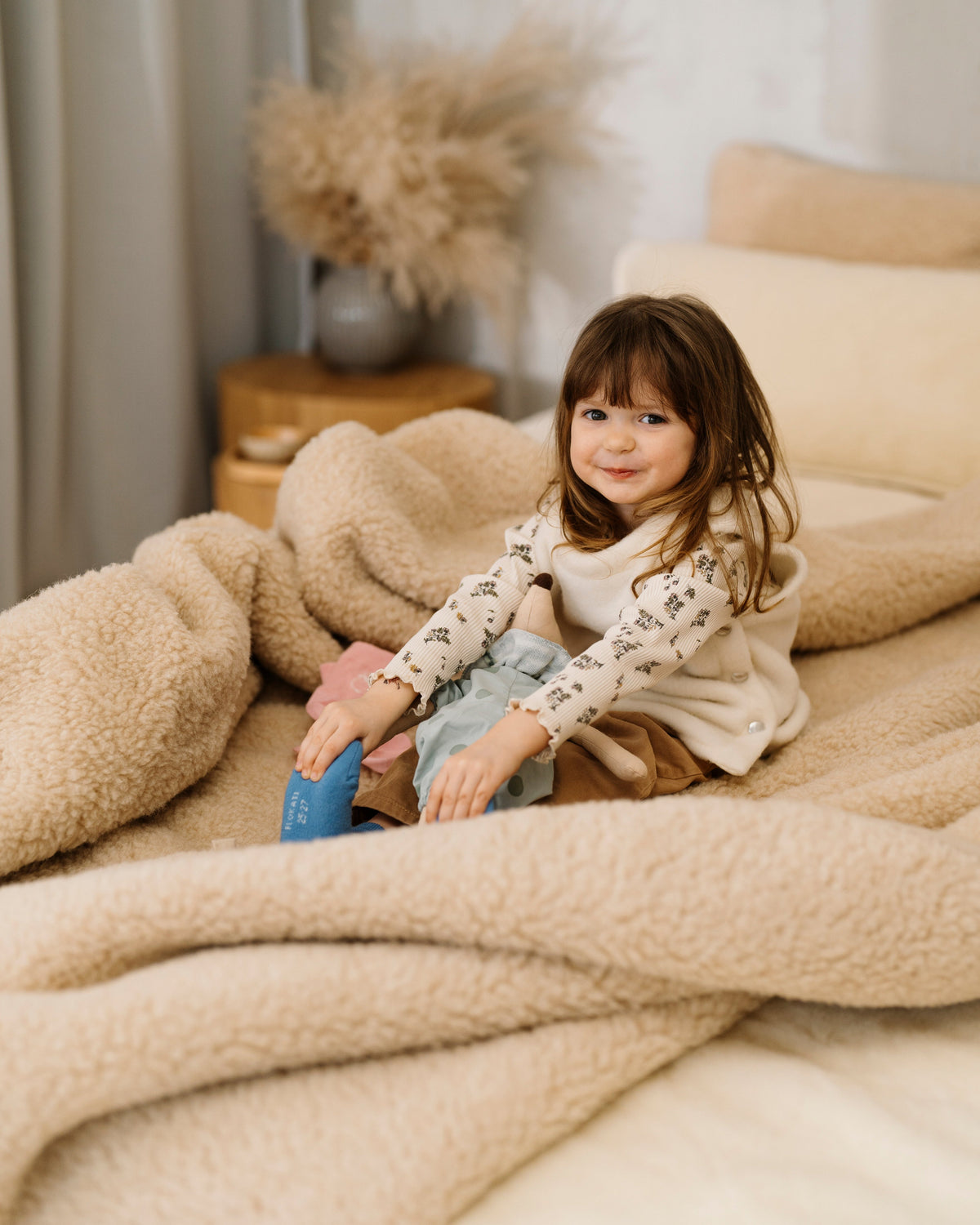 A child sitting on a bed under the Nut merino blanket