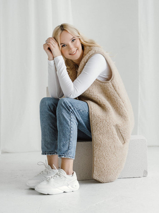 A woman sitting down in the Pearl merino vest in beige